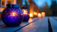 Purple glass lantern with glowing candle on wooden deck at dusk, creating romantic ambiance with soft bokeh lights in background. Perfect for seasonal decor.