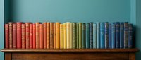 Colorful vintage books arranged by color spectrum on wooden shelf against turquoise wall creating rainbow gradient from red to blue for home decor and reading.