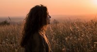 Young woman with curly hair enjoying peaceful sunset moment in golden wheat field during warm evening light for wellness and mindfulness concepts.