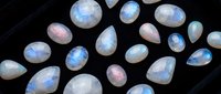 Luminous moonstone gemstones with iridescent blue and pink flashes arranged on dark surface. Natural precious stones for jewelry making and luxury accessories.