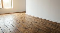 Empty room interior with rustic wooden plank flooring and white walls. Natural sunlight streaming through window creates warm atmosphere for home renovation.