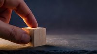 Hand placing wooden cube block on surface with dramatic lighting for business strategy and building concepts.
