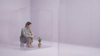 Young Asian businesswoman in gray suit sitting thoughtfully inside transparent glass cube with small plant in minimalist purple studio space.