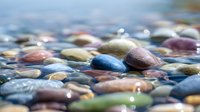 Colorful river stones underwater with shallow depth of field creating dreamy bokeh effect, ideal for nature and wellness backgrounds.