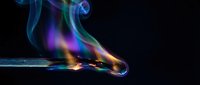 Colorful smoke rising from burning match with vibrant blue, green and purple flames against black background for creative design projects.