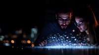 Young diverse business team analyzing glowing digital data visualization at night, modern technology concept showing futuristic interface with bokeh lights.