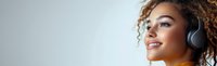 Young African American woman with natural curly hair wearing headphones and yellow top smiling while looking up, panoramic crop against light background.