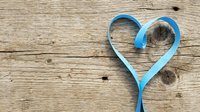 Blue ribbon heart shape on rustic wooden background with natural grain texture and knots for romantic greeting cards and love themed designs.