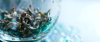 Loose leaf tea steeping in hot water with swirling motion, creating dynamic waves and steam clouds in glass cup for beverage preparation.