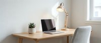 Clean minimalist home office workspace with laptop computer on wooden desk, adjustable brass lamp and gray chair near bright window for productivity and remote work.