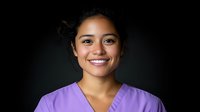 Young Asian healthcare worker wearing purple medical scrubs smiling warmly against dark background, representing wellness and professional care in medical settings.