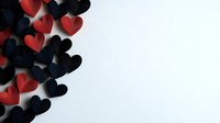 Red and black paper hearts scattered on white background creating modern minimalist composition with soft shadows and copy space for romantic message.