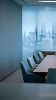 Modern conference room with wooden table, gray upholstered chairs, and floor-to-ceiling windows overlooking city skyline. Contemporary office interior design for corporate meetings and business presentations.