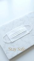 White disposable face mask on elegant marble surface with Stay Safe text, symbolizing health protection and pandemic safety awareness.