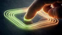 Hand touching glowing neon lines in green and orange, creating interactive light trails on dark surface for technology and innovation concepts.