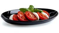 Fresh caprese salad with sliced tomatoes and mozzarella cheese garnished with basil leaves on black plate for Italian cuisine and healthy eating.