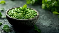 Fresh green guacamole dip garnished with cilantro leaves in rustic stone bowl on dark textured background with copy space. Traditional Mexican appetizer.