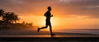 Runner jogging on wooden boardwalk at sunrise with tropical palm trees and ocean in background, silhouetted athletic person exercising outdoors.