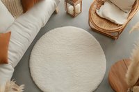 Cozy boho interior with round cream rug, rattan furniture, soft pillows and neutral decor elements creating minimalist scandinavian atmosphere.