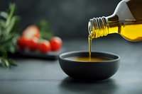 Pouring golden olive oil from bottle into black ceramic bowl on dark background with fresh rosemary and cherry tomatoes, food photography for cooking blogs.