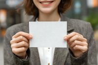 Young woman in gray blazer holding blank white card with smile, perfect for business presentation or announcement mockup.