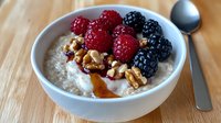 Creamy oatmeal bowl topped with fresh raspberries, blackberries, walnuts and honey drizzle on wooden table, healthy breakfast concept for food blogs.