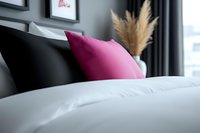 Modern bedroom interior with pink accent pillow on black leather headboard, white bedding and decorative pampas grass, creating cozy atmosphere.