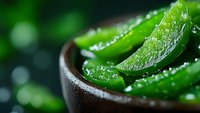 Fresh aloe vera plant leaves with water drops in wooden bowl on dark background, close up macro shot with selective focus and bokeh effect.