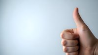 Hand showing thumbs up gesture against clean white background for positive feedback and approval concepts.