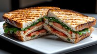 Fresh grilled sandwich with crispy toasted bread, layered with sliced turkey, bacon, lettuce, and tomato, cut diagonally and served on white plate.