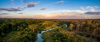 Aerial view of winding river flowing through dense forest landscape at golden hour sunset, showcasing natural waterway and lush woodland terrain for environmental and nature projects.