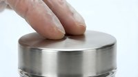 Hand touching smooth metallic cylinder surface with fingers making contact on brushed steel or aluminum material for industrial design concepts.
