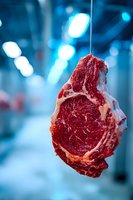 Raw beef ribeye steak hanging in meat processing facility with blue cold storage background, showcasing premium quality meat.