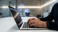 Businessman using laptop with artificial intelligence brain hologram in modern office workspace for technology innovation and digital transformation.