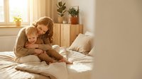 Young Caucasian mother hugging her toddler son on a cozy bed in a sunlit bedroom, sharing a warm tender moment of love and care.
