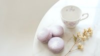 Lavender macarons on a marble table with a floral teacup and dried flowers, soft pastel aesthetic for food blogs and bakery menus.