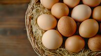 Fresh brown and beige chicken eggs in rustic nest with straw on wooden background, natural organic farm produce for healthy cooking and baking.