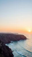 Dramatic coastal cliffs meet turquoise ocean waves at golden sunrise, with rocky headlands and distant islands visible on the horizon. Perfect for travel, nature, and landscape design projects.