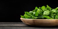 Fresh baby spinach leaves in wooden bowl on dark rustic table against black background, healthy organic greens for cooking and salads.