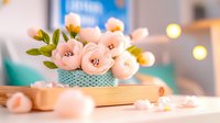 Delicate pink paper flowers in turquoise polka dot vase on wooden surface with warm bokeh lights creating cozy crafting atmosphere for DIY projects.