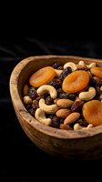 Mixed nuts and dried fruits in rustic wooden bowl on dark background for healthy snacking and cooking ingredients.