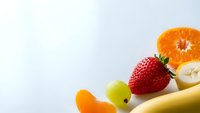 Fresh colorful fruits including strawberry, banana, orange slice and grapes arranged on white background with copy space for healthy eating concepts.