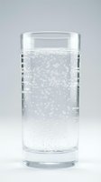 Glass of sparkling water with rising bubbles on a light gray background, conveying freshness and hydration for health and beverage concepts.