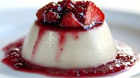 Creamy vanilla panna cotta dessert topped with fresh berry sauce and mixed berries on white plate, close up view of Italian cuisine delicacy.