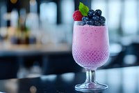 Pink berry smoothie topped with fresh raspberries and blueberries in crystal glass on dark surface against blurred restaurant background. Garnished with mint leaf.