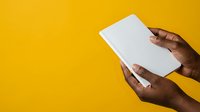 Close-up of dark-skinned hands holding blank white tablet against vibrant yellow background. Suitable for technology, business, app development, digital marketing, and modern lifestyle concepts.