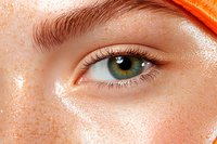 Close-up macro shot of green eye with natural freckles and long eyelashes on light skin with orange accent detail, showing natural beauty and youth.