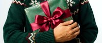 Person wearing dark green knit sweater holding wrapped gift box with red ribbon bow, cropped torso view for holiday shopping and seasonal celebration themes.