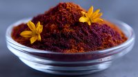 Red saffron powder in glass bowl decorated with yellow flowers on dark background, aromatic eastern spice for cooking and natural food coloring.