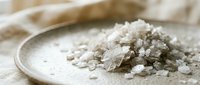 Coarse sea salt crystals piled on a ceramic plate with linen fabric, suitable for culinary, food styling, seasoning, and cooking ingredient applications.